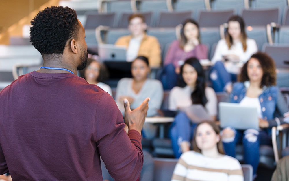 Rear view of Black male speaking to students in an auditorium setting.