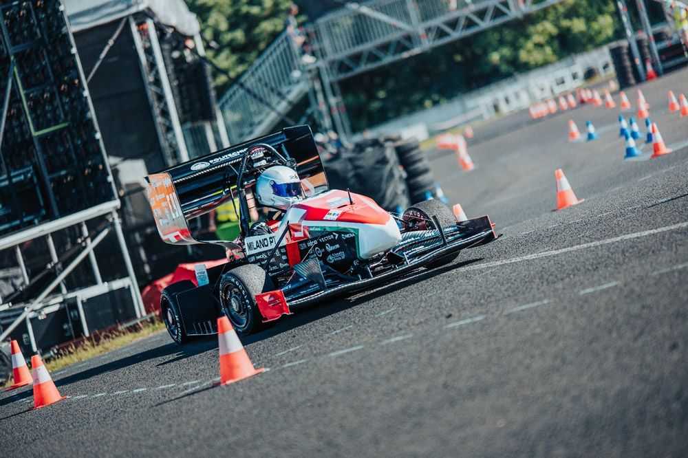 A driver tests the Dynamis PRC Formula SAE vehicle on an empty stretch of a racetrack blocked off by cones.